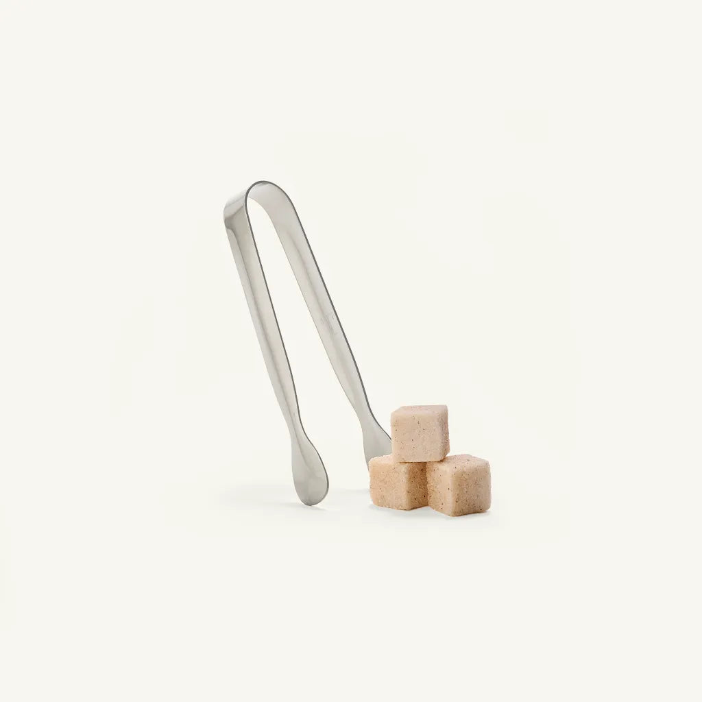 Metal tongs with sugar cubes on a white background