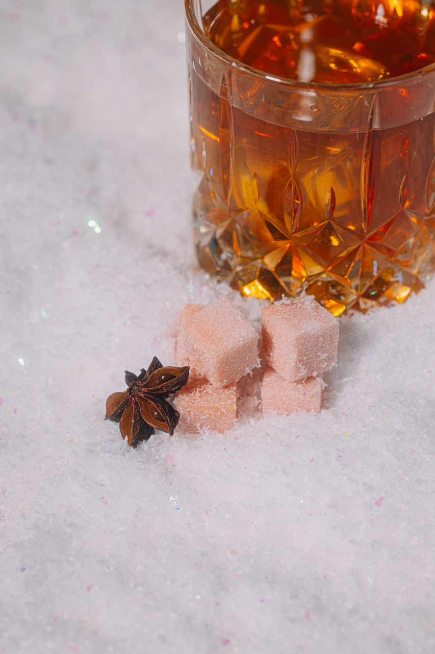 Glass of amber bourbon with star anise and Luxe Mixer Cubes on a snowy surface