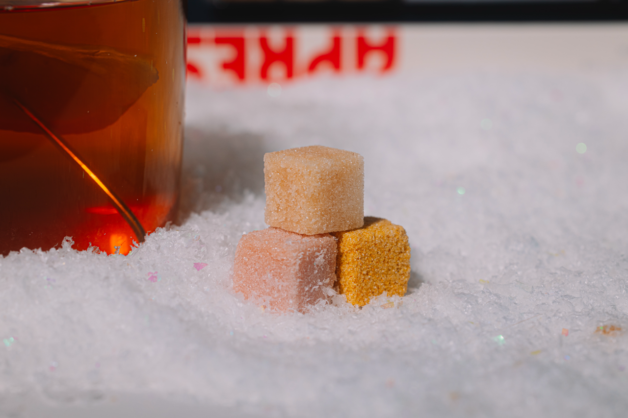 Three Luxe mixer cubes stacked on a snowy surface with a blurred bottle of alcohol in the background.