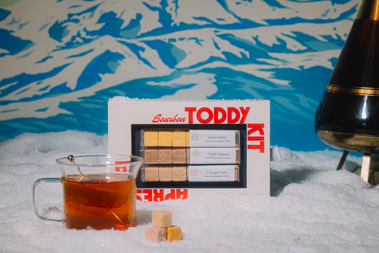 Bourbon Toddy Kit with a glass of amber liquid on a snowy background
