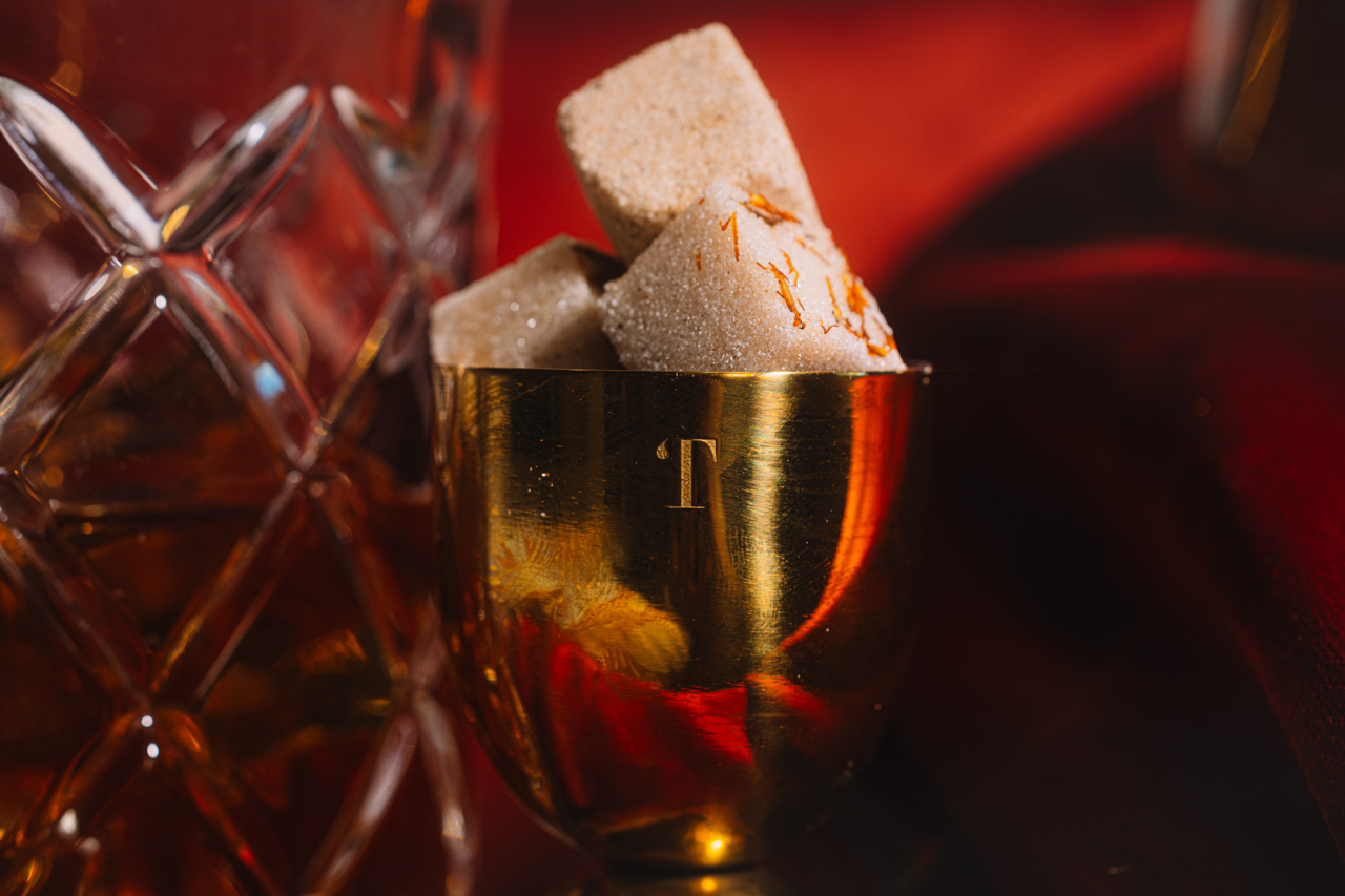 Gold Jigger filled with LUXE Mixer Cubes on a dark red background