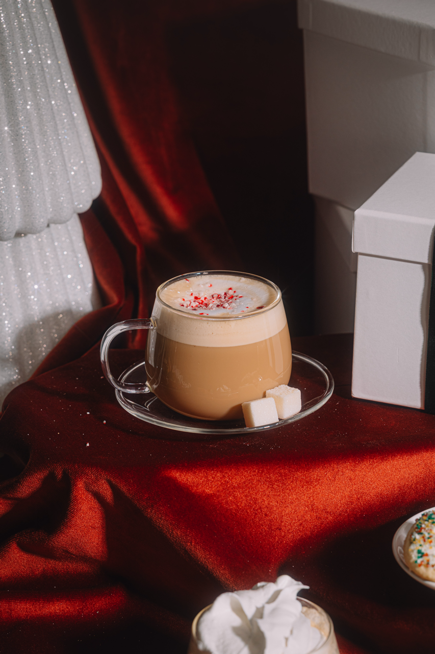 Cappuccino with whipped cream and a small gift box on a red surface