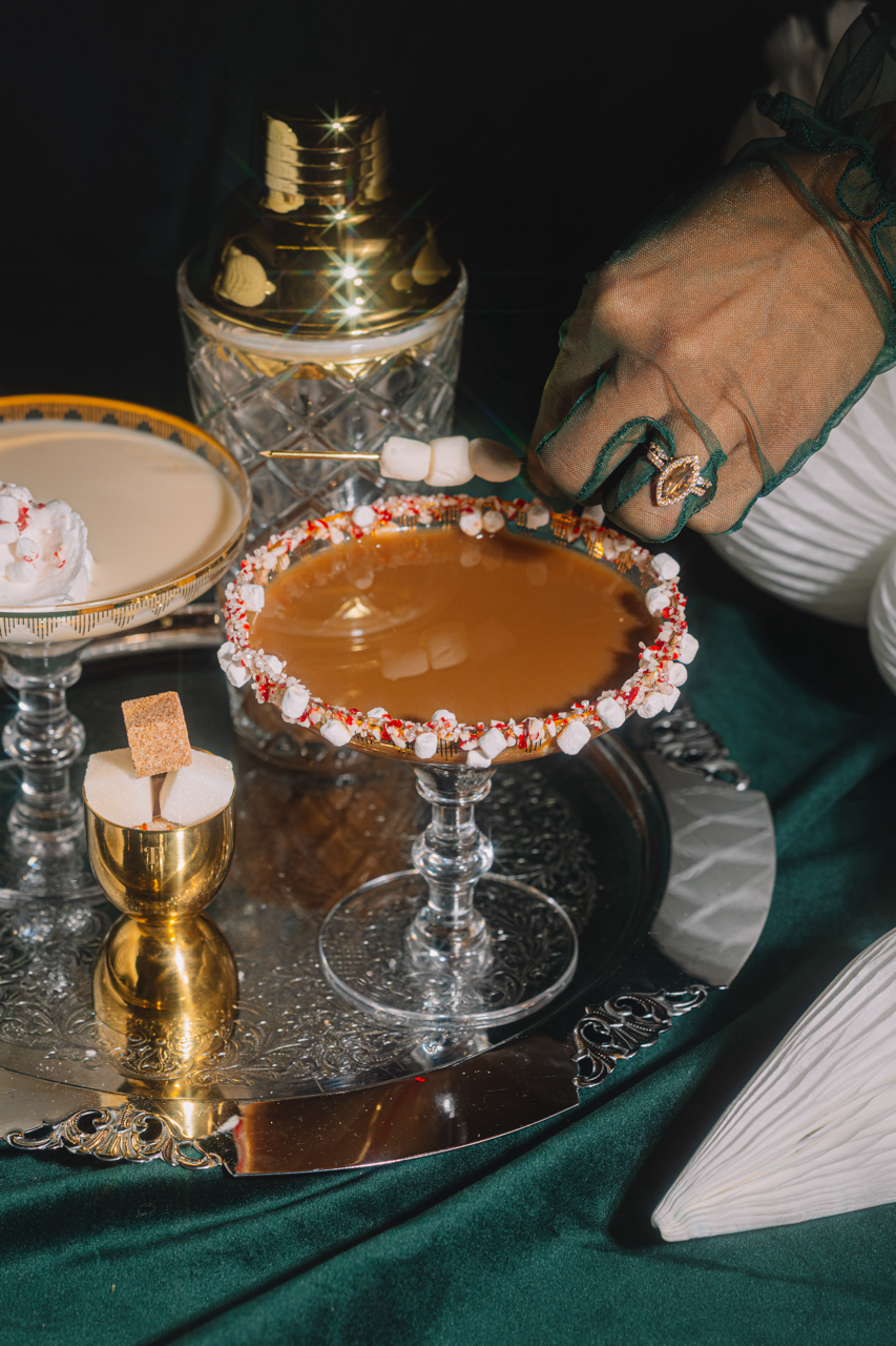 Decorative cocktail with a rim of candy and whipped cream, served on a reflective surface.