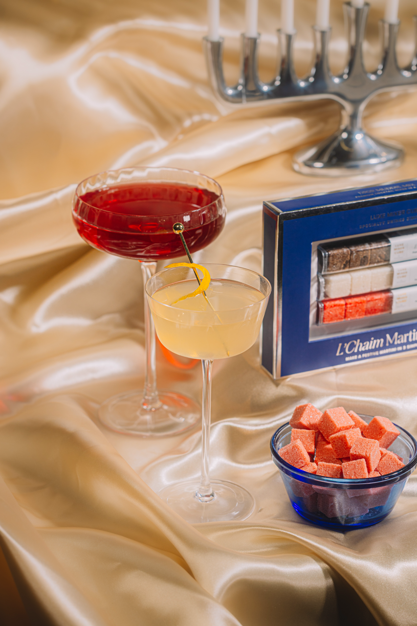 Two cocktails on a table with a box of L'Chaim Martinis and a bowl of watermelon cubes.