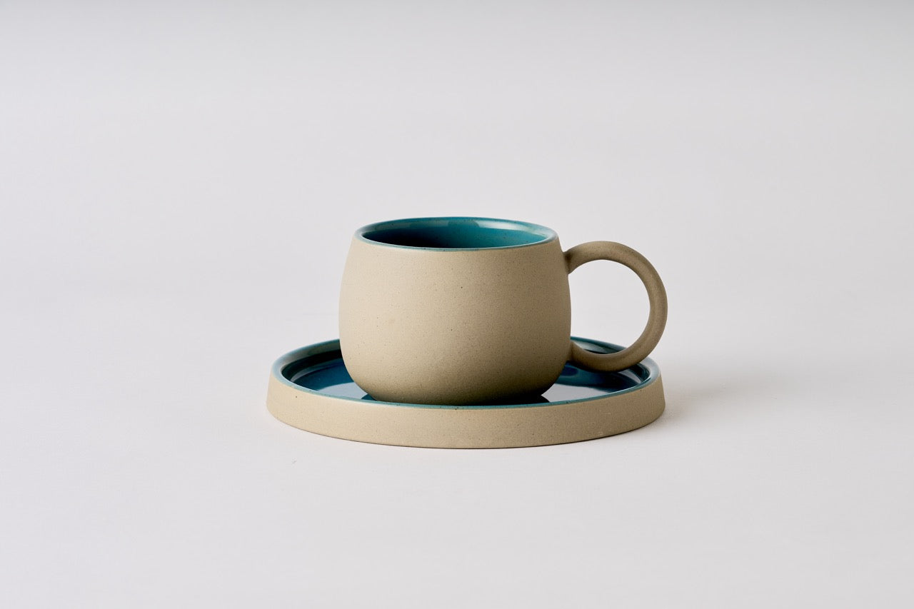 Ceramic mug with teal interior on a matching saucer against a light gray background