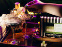A hand garnishes a cocktail with a sliced apple on a skewer over smoky martini glasses, with a branded box reading 'Poison Apple Martini' and a clapperboard in the background under dramatic purple lighting.