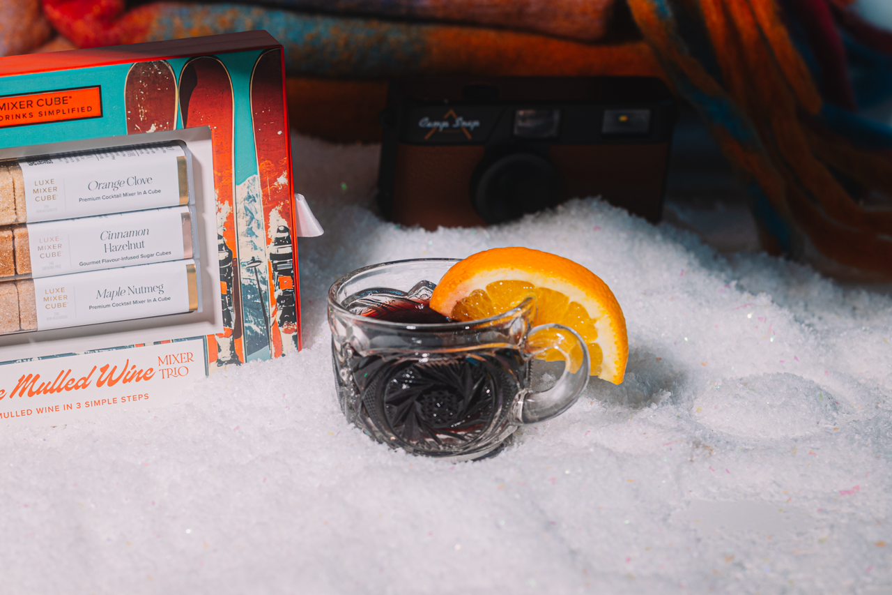 Hot mulled wine with orange slice in a mug, mulled wine box, and camera in the snow