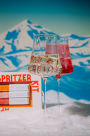 Two glasses of sparkling wine with a mountainous background and Spritzer Kit packaging.