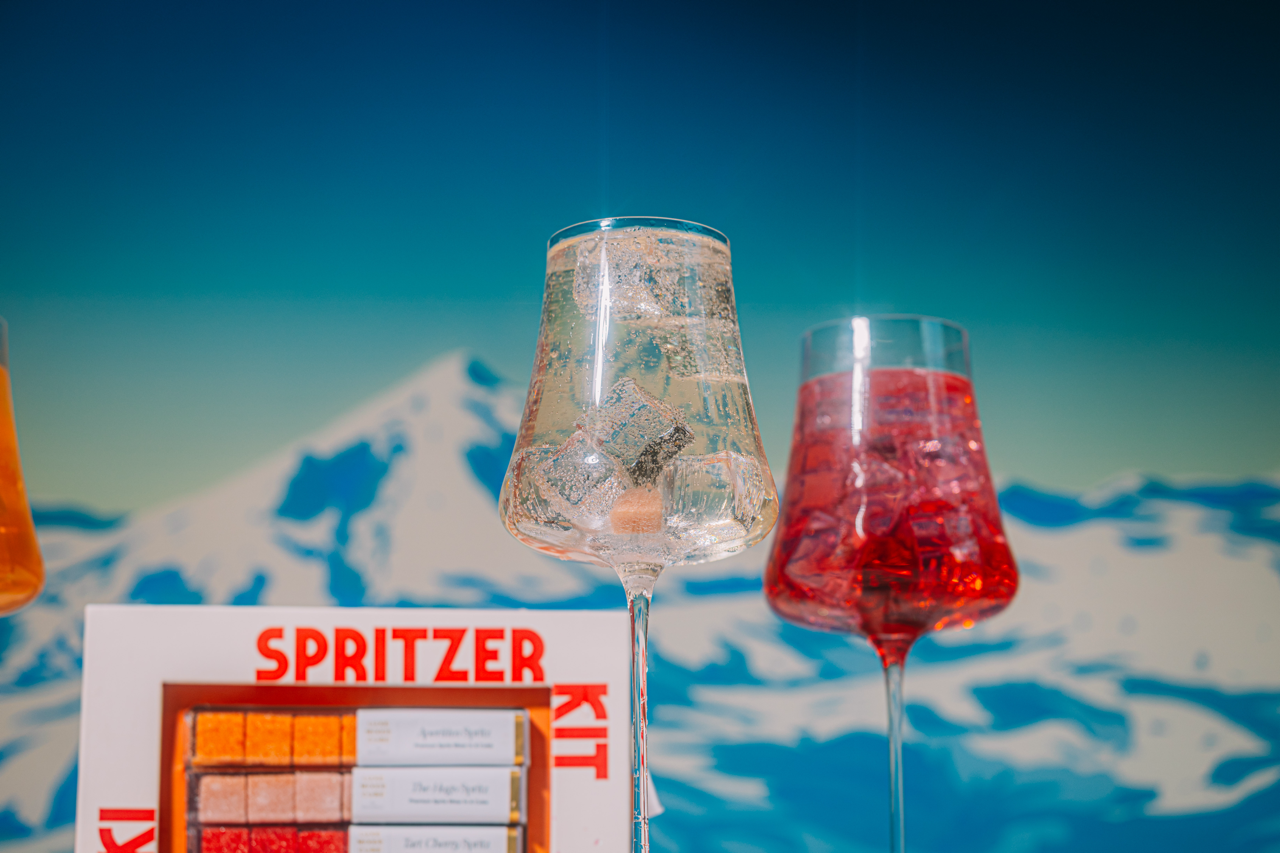 Two glasses of spritzers with a mountainous background and Spritzer Kit packaging.