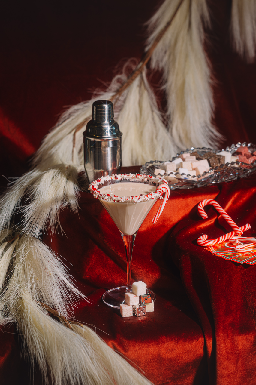 Christmas-themed cocktail with candy cane garnish on a red tablecloth.