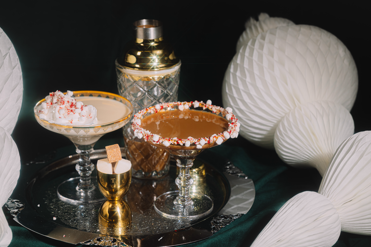 Two cocktail glasses with candy rims on a tray, surrounded by decorative elements.