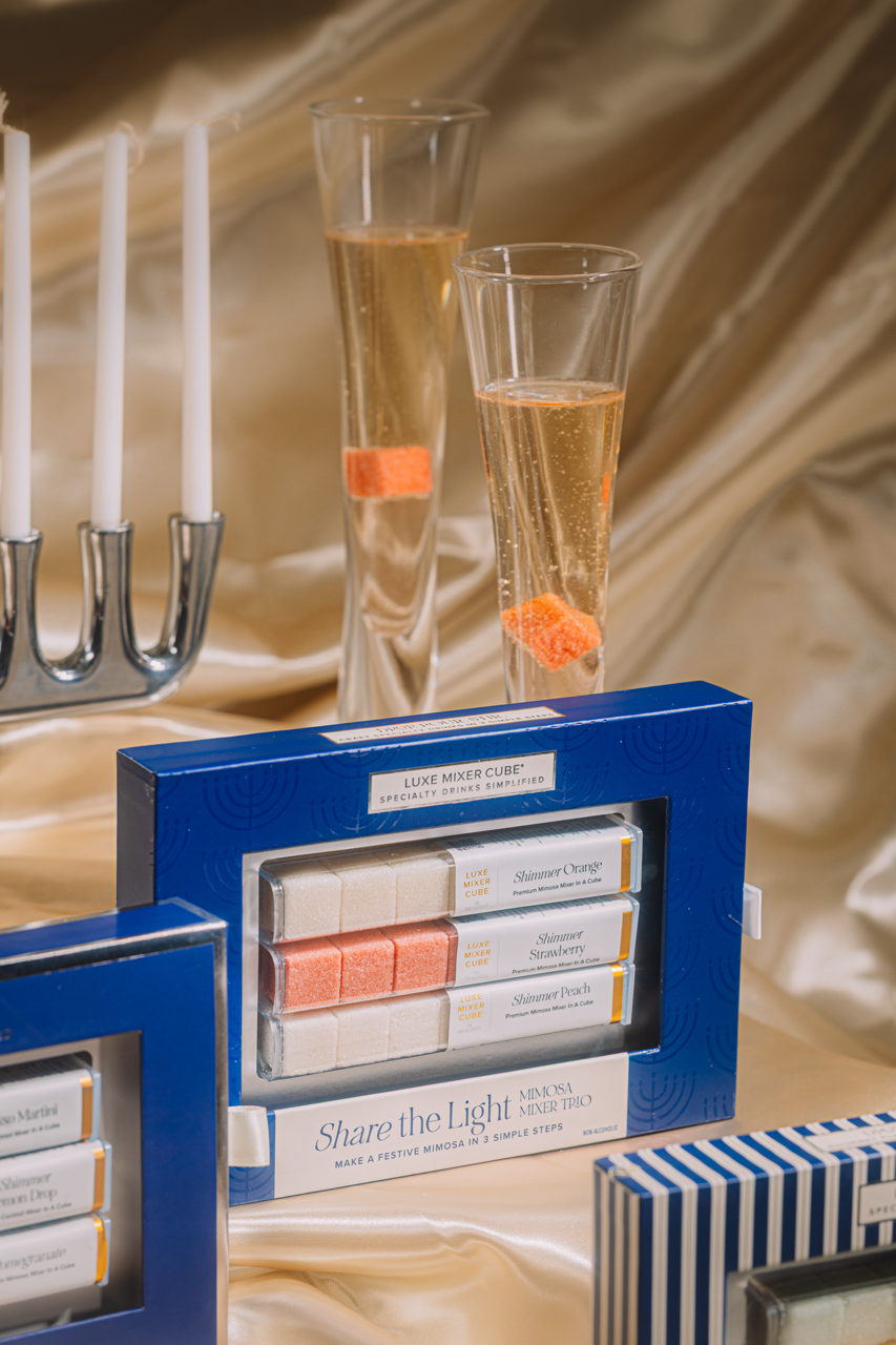 Two glasses of champagne with orange candies, a menorah, and a box of candles on a gold fabric background.