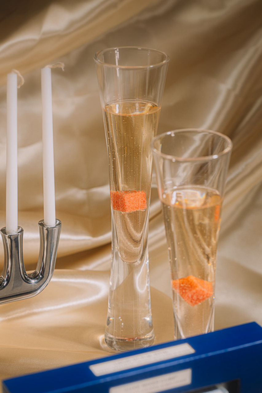 Two tall glasses with orange slices and white wine on a reflective surface.